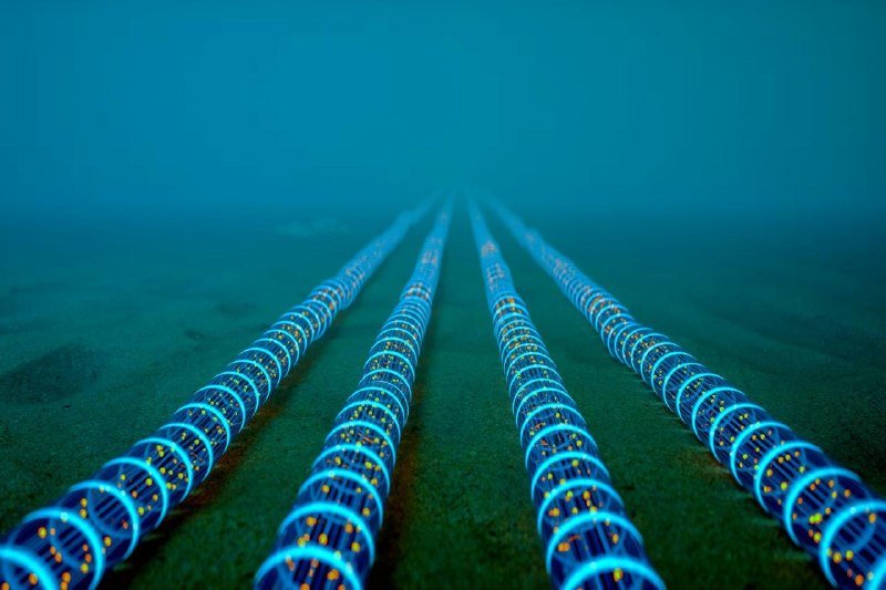 Four illuminated cylindrical cables with glowing blue rings and orange lights run parallel across a greenish seabed, vanishing into a hazy turquoise underwater background in this digital illustration.