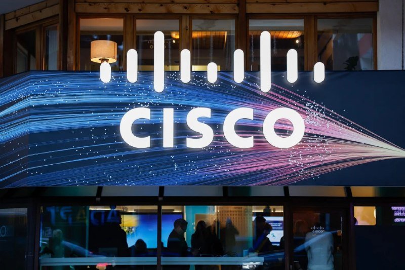 An illuminated Cisco logo and branding display glows above a glass-fronted entrance where silhouettes of people are visible inside.