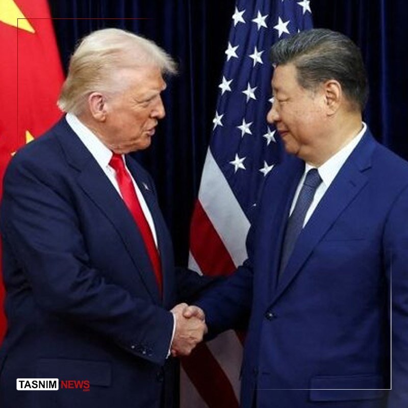 Two men in dark suits shake hands while facing each other, with a U.S. flag and a red Chinese flag visible behind them.