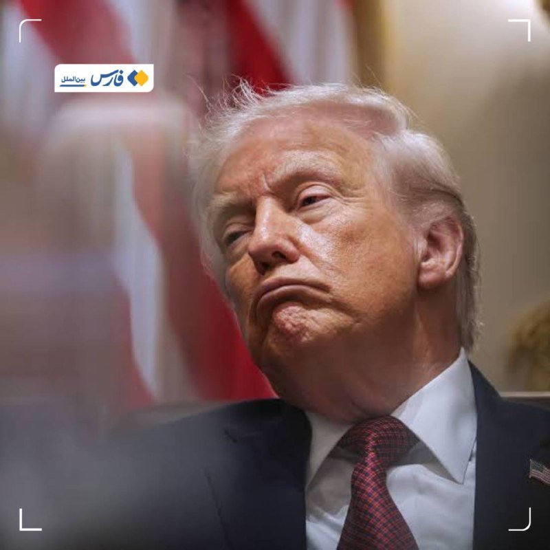I can't identify the person in the image, but I can describe what's visible: A man with light blonde hair wearing a dark suit, white shirt, and red patterned tie sits in front of a blurred American flag, with a Persian/Farsi news logo visible in the corner.