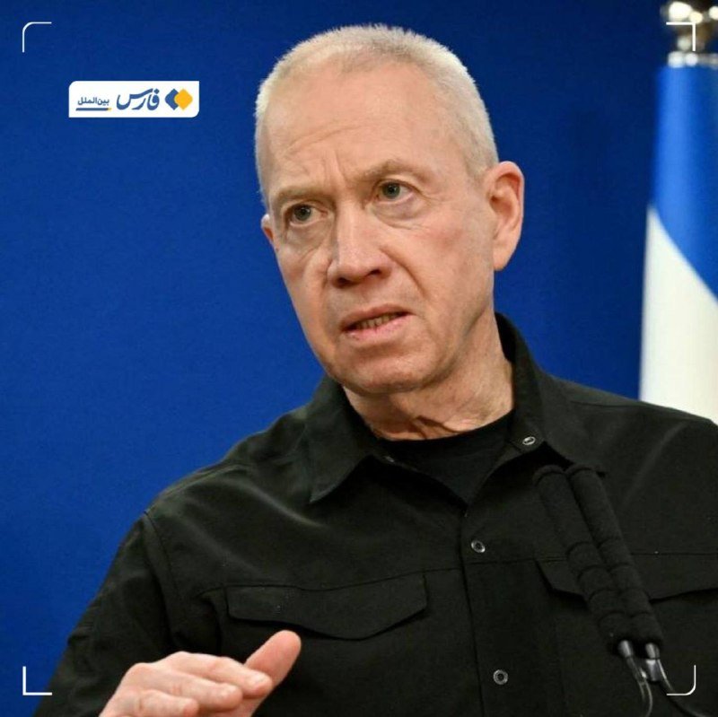 An older man with short gray hair in a black shirt speaks, gesturing with his hand in front of a blue backdrop with a flag.