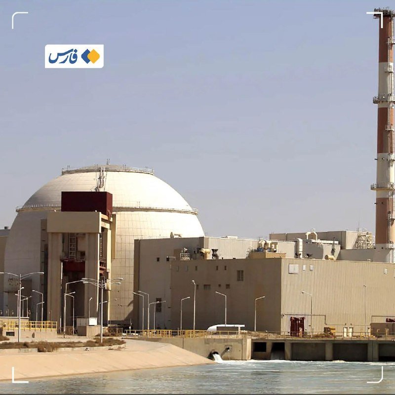 A nuclear power plant with a large white dome containment building and adjacent industrial structures sits along a coastline, with water discharging from an outfall pipe in the foreground.
