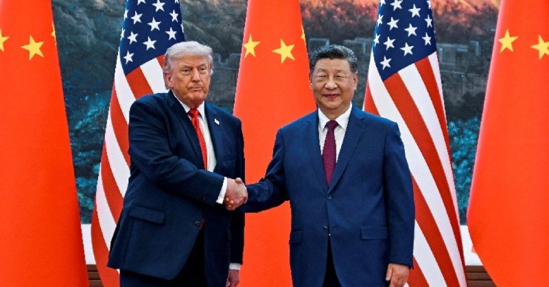 Two men in dark suits shake hands in front of alternating United States and Chinese flags.