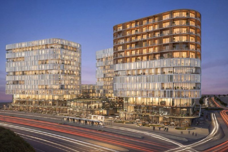 Architectural rendering of illuminated multi-story glass buildings with curved facades at dusk, featuring ground-floor retail and blurred vehicle light trails along an adjacent roadway.