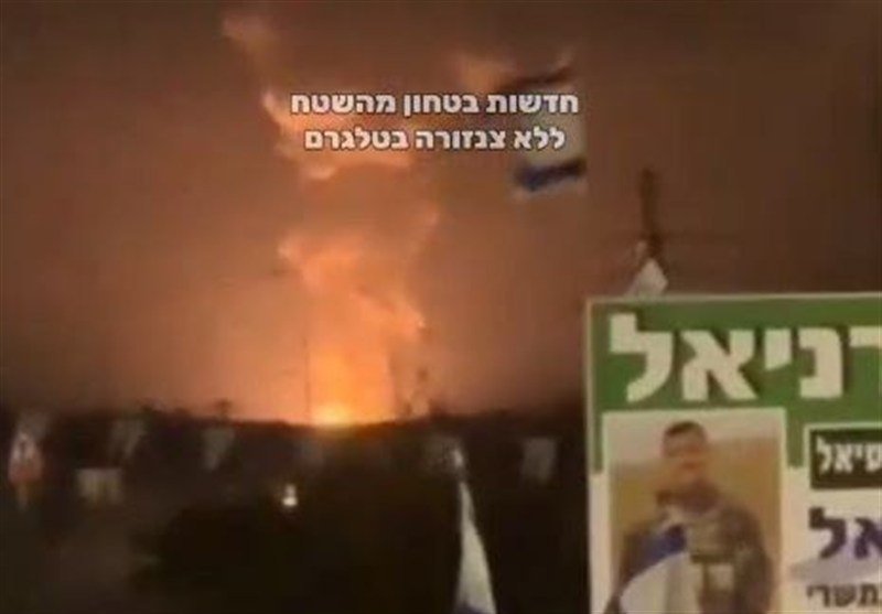 A large fire burns at night with billowing smoke, an Israeli flag visible, and Hebrew text reading "מדשות בטחון מרשת ללא צנזורה בטענמ" overlaid on a green sign.