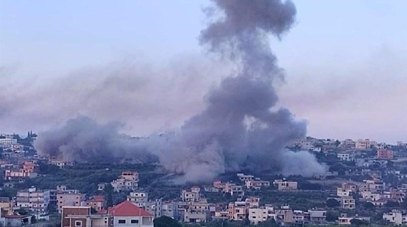 Thick plumes of gray smoke rise above a hillside residential area filled with densely packed houses under a hazy sky.
