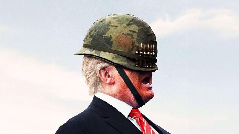 A man in a dark suit and red tie is shown in profile wearing a camouflage military helmet with a chin strap fastened, against a pale sky.