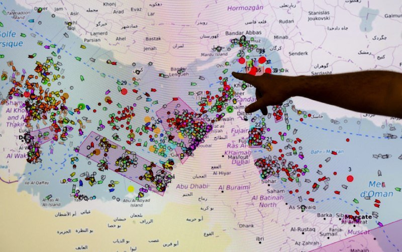 A hand points to a map of the Persian Gulf region covered with numerous colored markers indicating locations across cities including Dubai, Abu Dhabi, and Bandar Abbas.