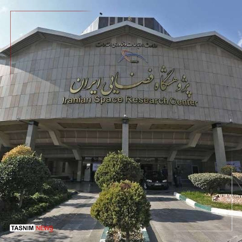A large concrete building displays signage reading "Iranian Space Research Center" in English and Persian script, with a dark vehicle parked at the covered entrance beneath manicured shrubs.