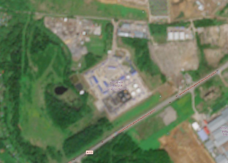 Aerial/satellite image showing an industrial facility with cylindrical tanks, storage containers, and surrounding green vegetation, intersected by a road marked "A-113."
