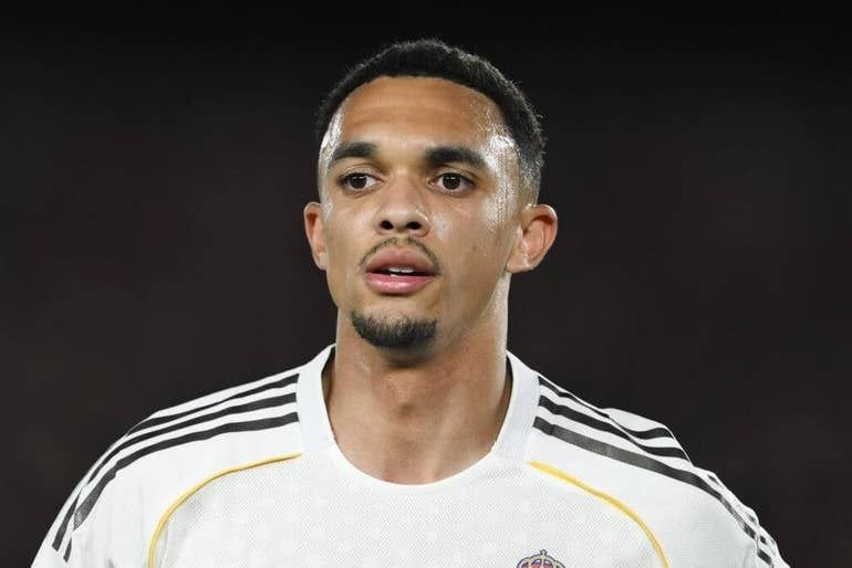 A young soccer player in a white jersey with black shoulder stripes looks off to the side against a dark background.
