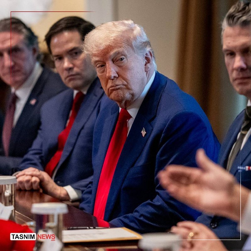 Several men in suits, including a blonde-haired man in a navy suit and red tie, are seated at a table during what appears to be a meeting.