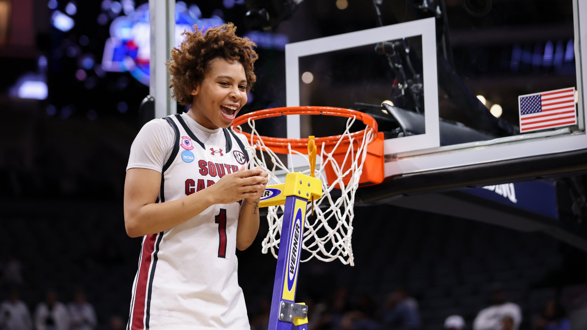 South Carolina basketball player wearing #1 jersey smiles while cutting down the net after a championship game.