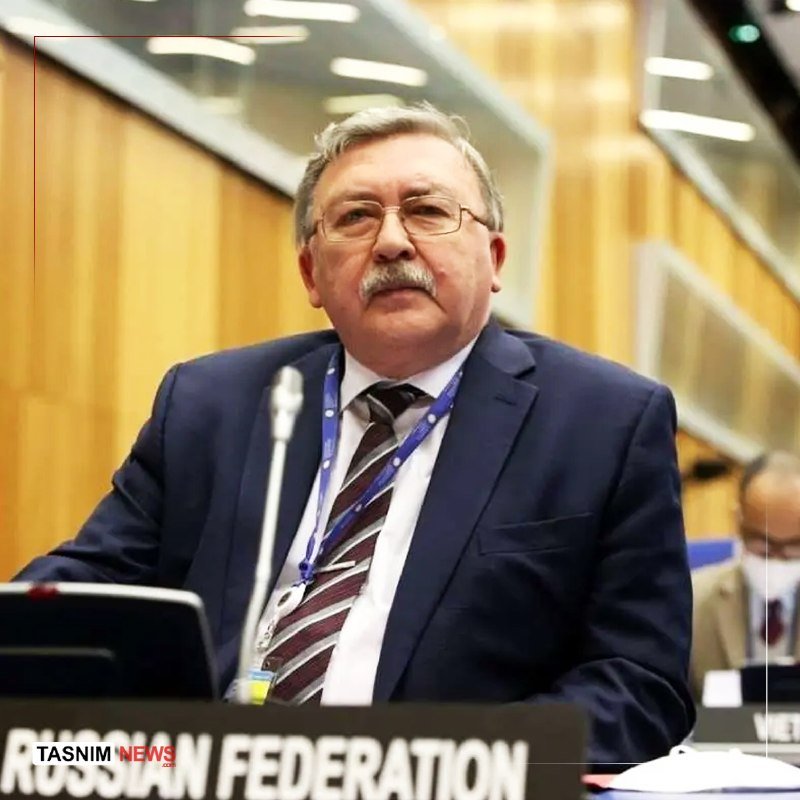 A man in a dark suit and striped tie sits at a desk with a "RUSSIAN FEDERATION" placard and microphone, with the Tasnim News logo in the corner.