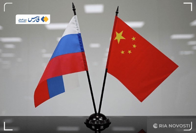 Two small flags—the Russian tricolor and the Chinese flag with yellow stars—stand crossed on a black base against a gray background, with a "RIA Novosti" logo in the corner.
