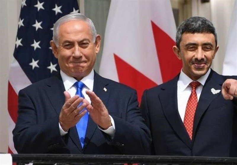 Two men in suits stand smiling in front of the U.S. and Canadian flags, with one clapping and the other pointing toward the camera.