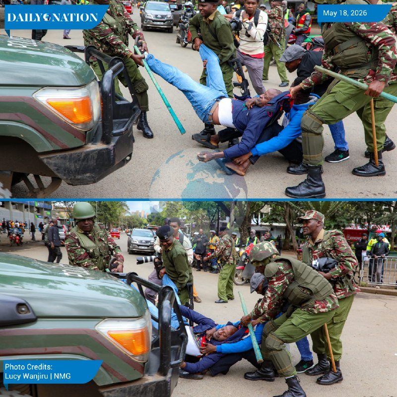 Uniformed personnel in camouflage drag a man across a street next to a military-style vehicle during a daytime confrontation.