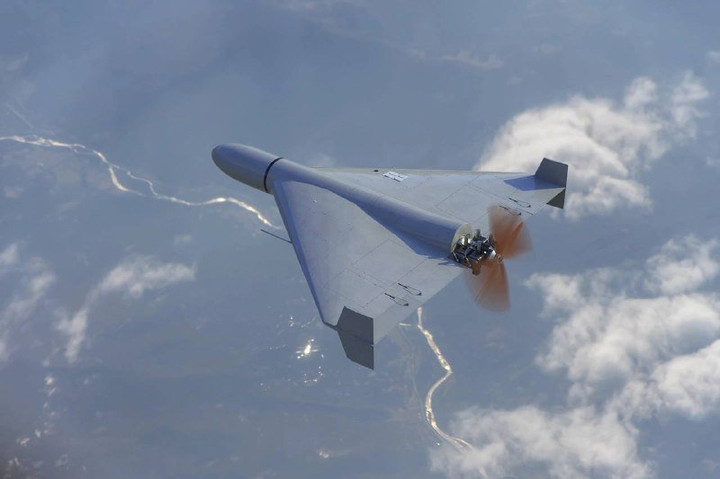 A delta-wing unmanned aircraft with an exposed rear propeller flies above clouds and mountainous terrain.