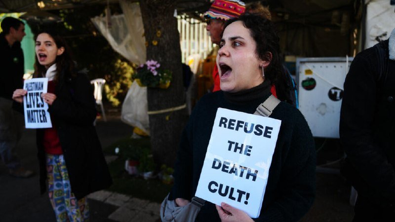Protesters chant and hold signs reading "REFUSE THE DEATH CULT!" and "A MOTHER LOVES MATTER" during an outdoor demonstration.