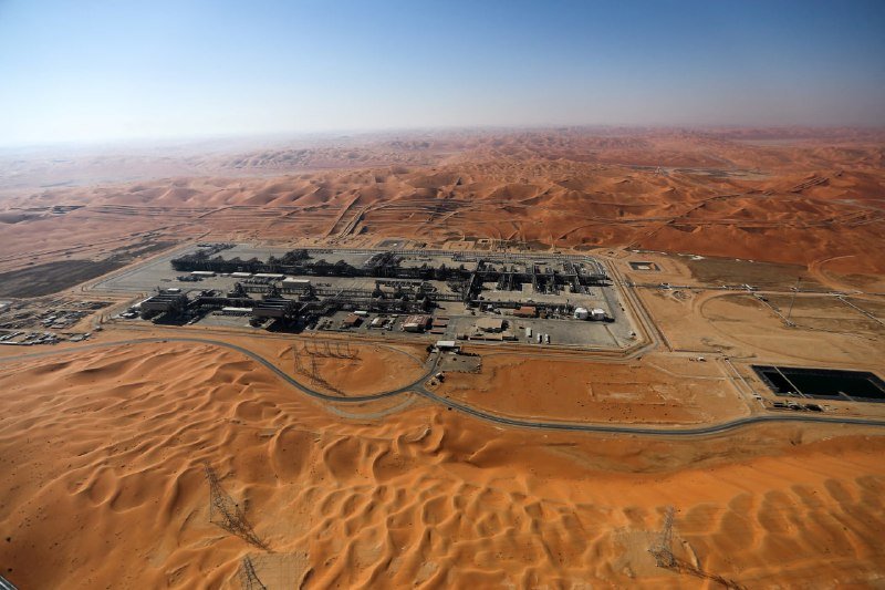 Aerial view of an industrial facility surrounded by orange sand dunes in a vast desert.