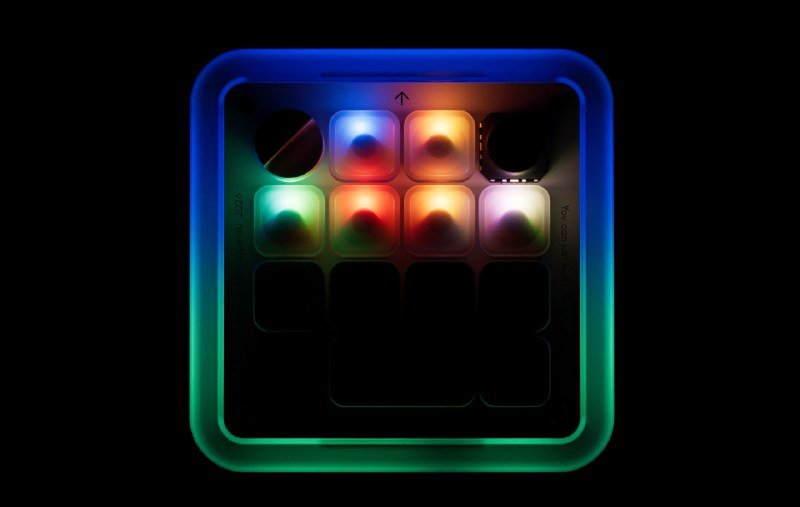A square electronic device with a glowing blue and green border and an illuminated grid of colored buttons sits against a black background.