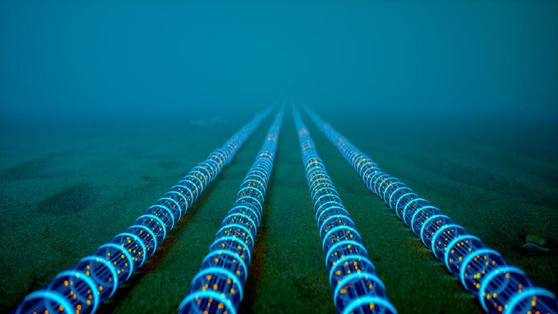 Multiple glowing blue-and-yellow patterned cables lie parallel on a sandy seabed, extending into murky underwater distance.