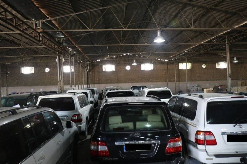 Rows of SUVs and minivans are parked tightly inside a large warehouse with a high metal-truss ceiling, brick walls, and overhead lighting.