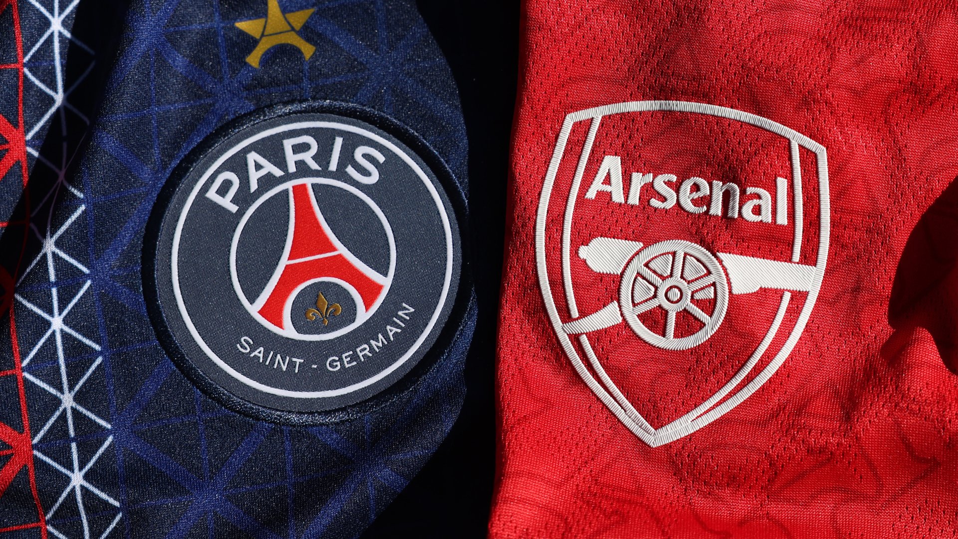 Close-up showing the Paris Saint-Germain and Arsenal football club crests side by side on dark blue and red fabric jerseys.