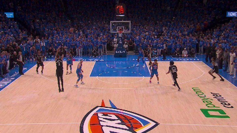 A basketball player shoots a free throw on a court featuring an "OKC" center logo, surrounded by a crowd wearing blue shirts.
