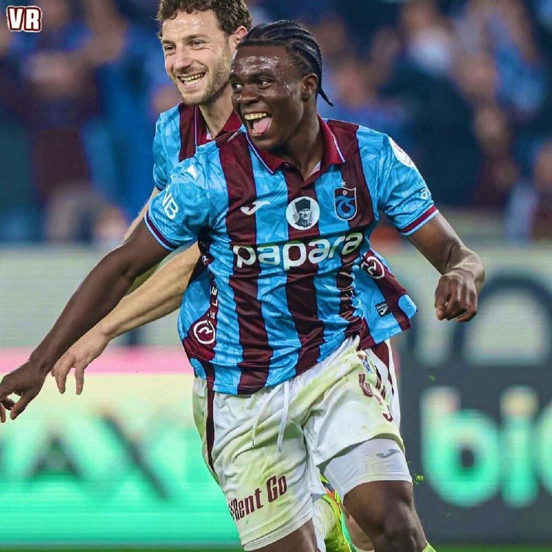 Two soccer players in blue and claret striped jerseys with "papara" printed on the front celebrate on the pitch, smiling broadly.