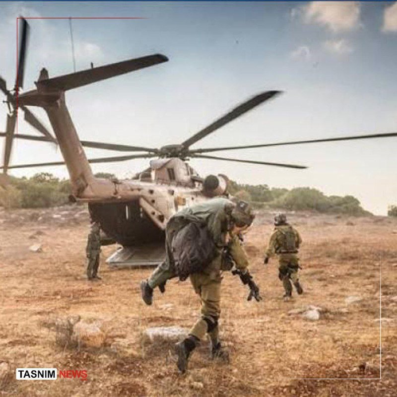 Soldiers in camouflage uniforms run across a dry, grassy field toward a large military helicopter with spinning rotors.