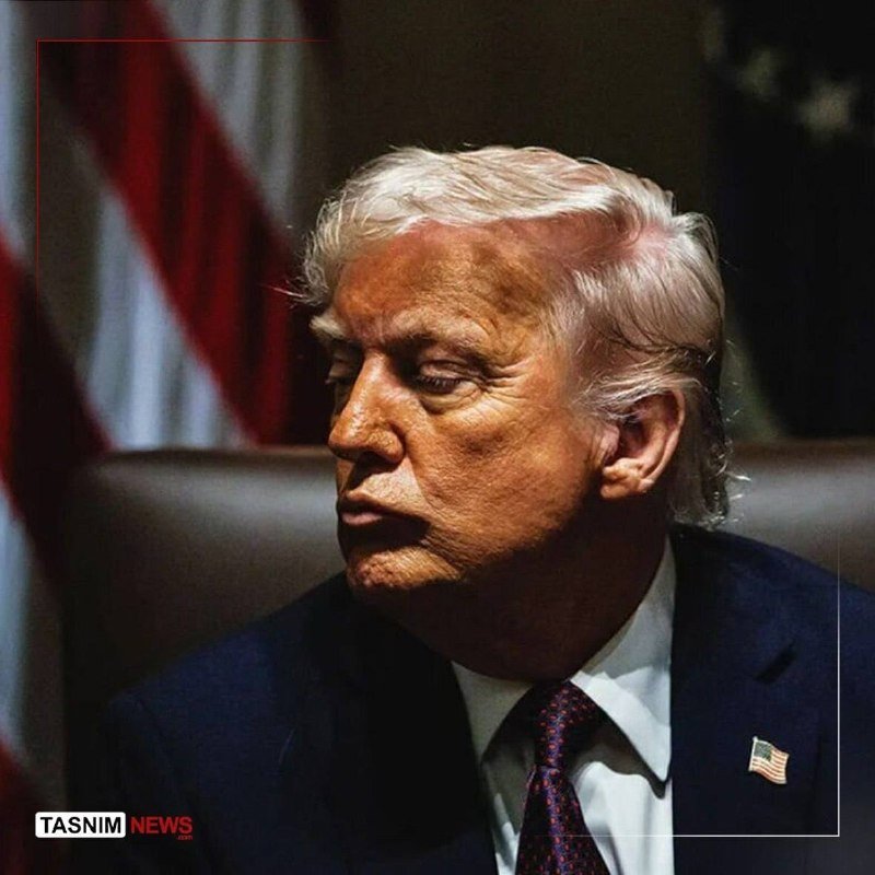 A man with blonde hair in a dark suit and tie sits before an American flag, with "TASNIM NEWS" visible in the corner.