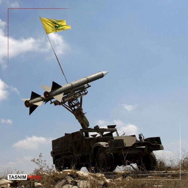 A military truck-mounted missile launcher with two surface-to-air missiles angled upward sits in a rocky field under a partly cloudy sky, a yellow flag mounted on a tall pole waving above.