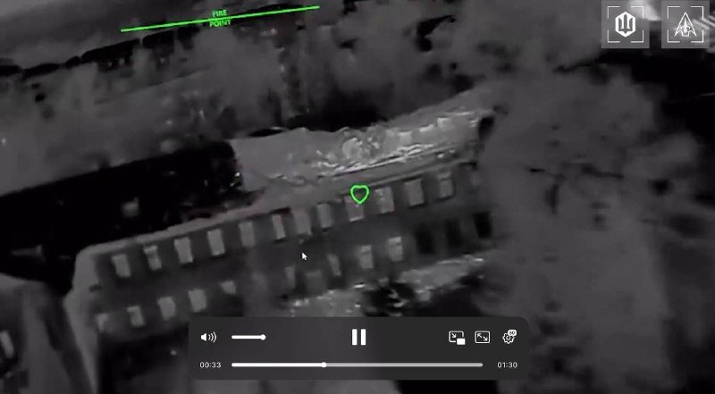 Aerial thermal-style video footage shows a damaged building with a green targeting marker and a video player interface overlay.