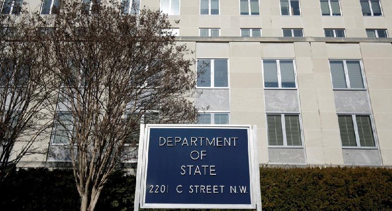 A blue sign reading "DEPARTMENT OF STATE, 2201 C STREET N.W." stands in front of a multi-story stone office building with rows of windows.