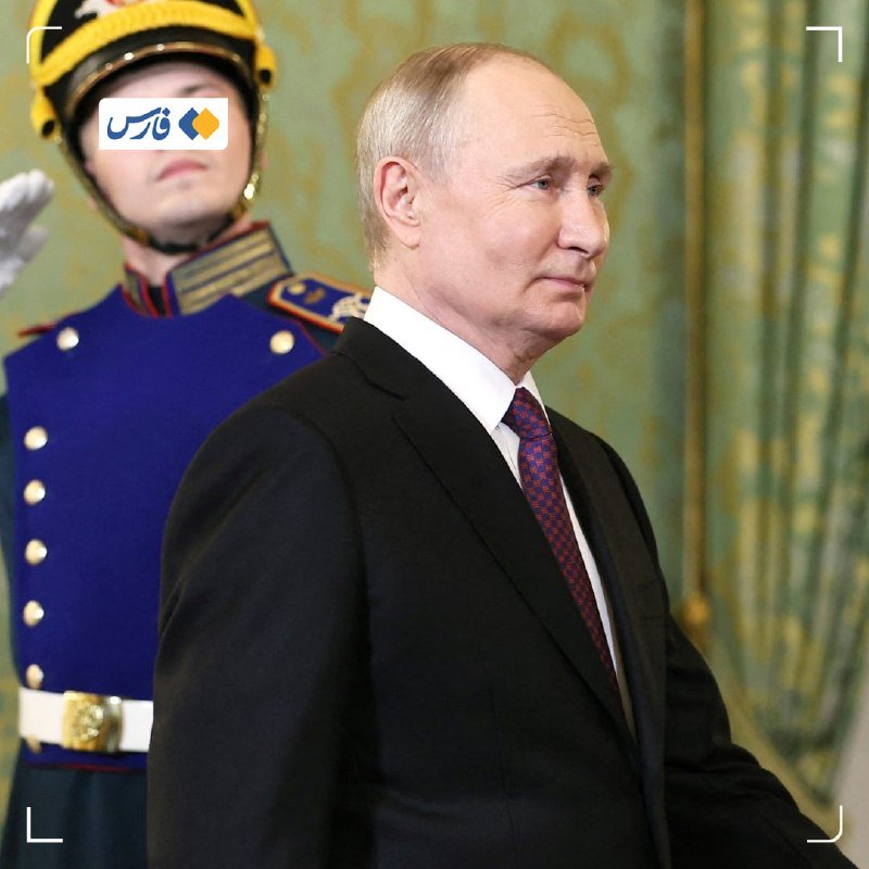 A man in a black suit and red patterned tie stands in an ornately decorated room, with a uniformed guard in a blue tunic and plumed helmet positioned behind him.