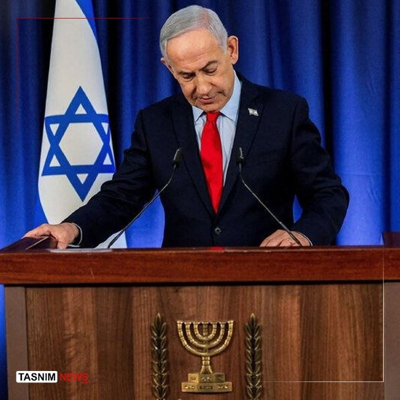 A man in a dark suit and red tie stands at a wooden podium bearing a menorah emblem, with an Israeli flag visible behind him.