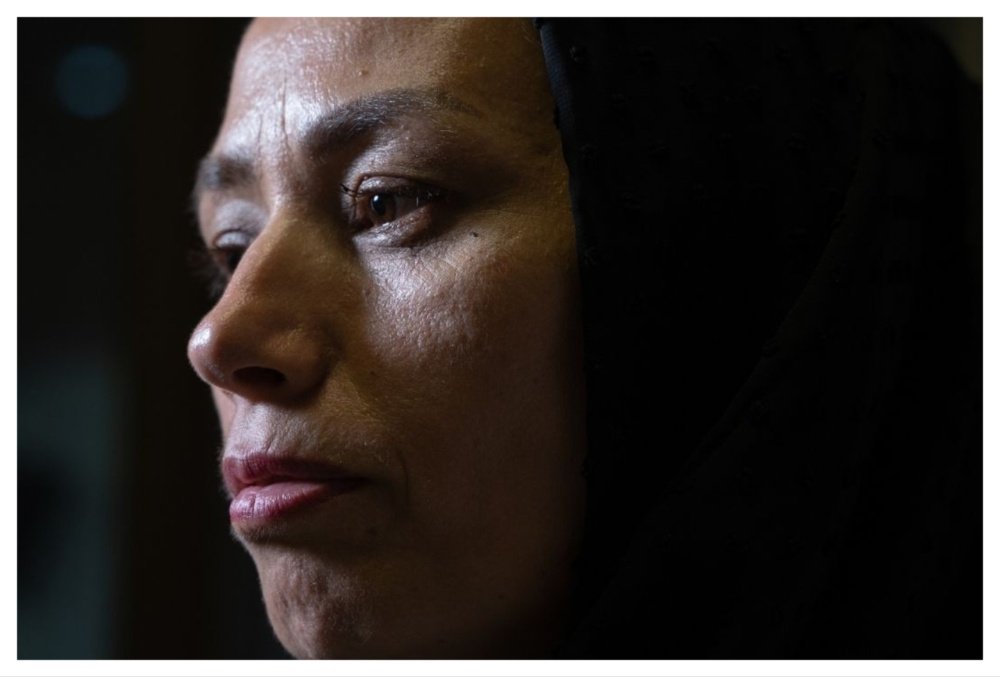 A close-up profile photo shows a person wearing a black head covering, gazing off to the left against a dark background.
