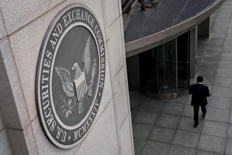 A man in a dark suit walks on a paved plaza beside a stone building displaying the U.S. Securities and Exchange Commission seal featuring an eagle and "MCMXXXIV."