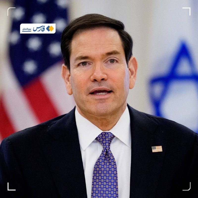 A man in a dark suit, white shirt, and blue patterned tie speaks, with an American flag and a blue Star of David emblem visible in the background.