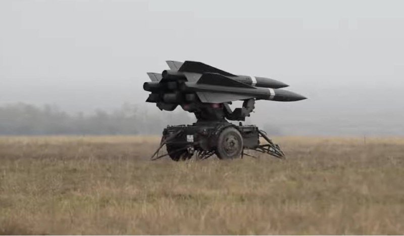 A military surface-to-air missile launcher on wheels sits in a grassy field under an overcast sky, its missiles elevated and pointed skyward.