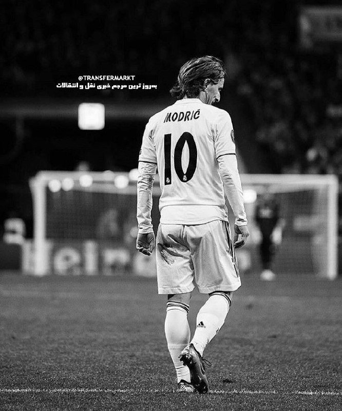 Black-and-white image shows a soccer player wearing a jersey labeled "MODRIĆ" and number 10, walking on a pitch with a goal and another player visible in the background.