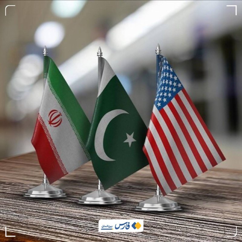 Three small desk flags—Iran, Pakistan, and the United States—stand side by side on a wooden surface.