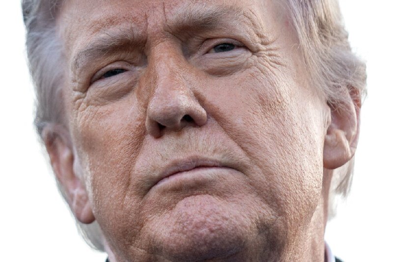 Close-up portrait of an older man with blond hair and a stern expression against a white background.