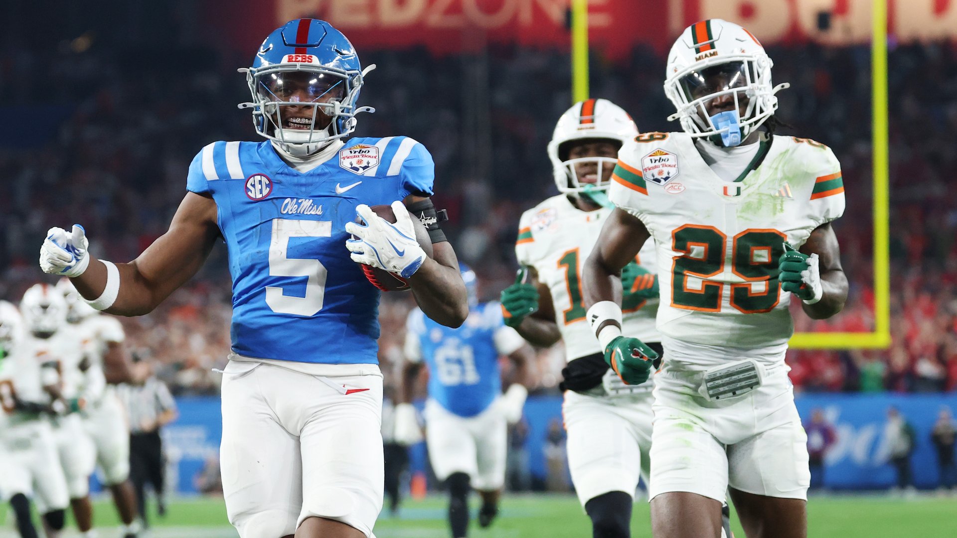 An Ole Miss football player wearing jersey number 5 carries the ball while being pursued by two Miami players in white and orange uniforms during a football game.