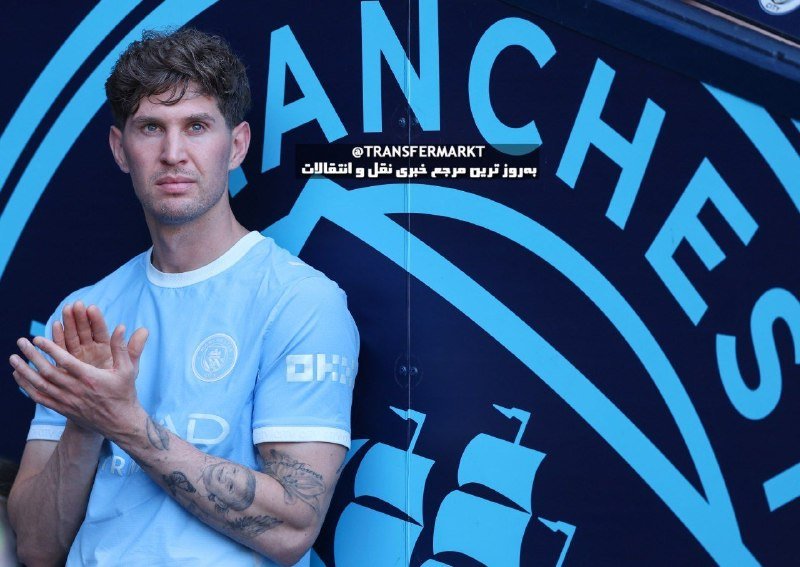 A man in a light blue soccer jersey claps while standing in front of a dark blue backdrop featuring large light blue "MANCHESTER" lettering.