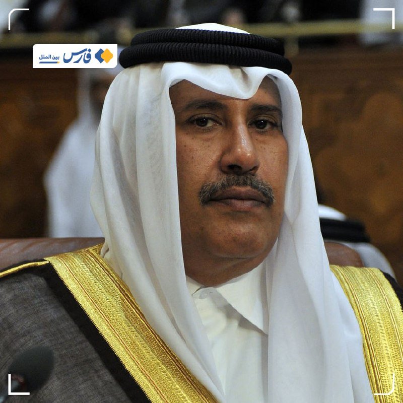 A man wearing a white keffiyeh with black agal and a gold-trimmed bisht sits in a formal indoor setting.