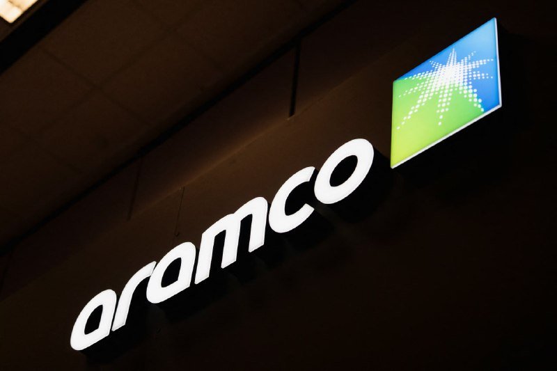 An illuminated "aramco" sign with a green and blue starburst logo is mounted on a dark exterior wall at night.