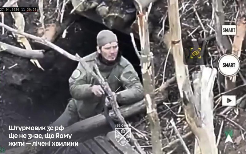 A soldier in military gear and a beanie emerges from a dark dugout surrounded by broken tree branches and debris, as shown in a dated video still.