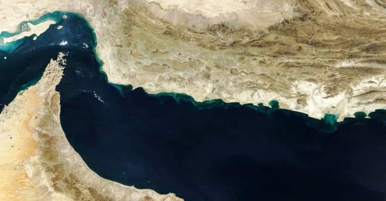 A satellite image shows a dark blue body of water bordered by arid, tan-colored land with rugged terrain along the coastline.